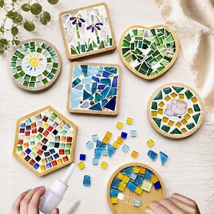 Può includere: Una collezione di sottobicchieri a mosaico colorati in varie forme, tra cui rotondi, quadrati, a cuore ed esagonali. Ogni sottobicchiere presenta un design unico con tessere di vetro nei toni del verde, blu, giallo e rosso. È presente anche un flacone di colla e piccole tessere di vetro.