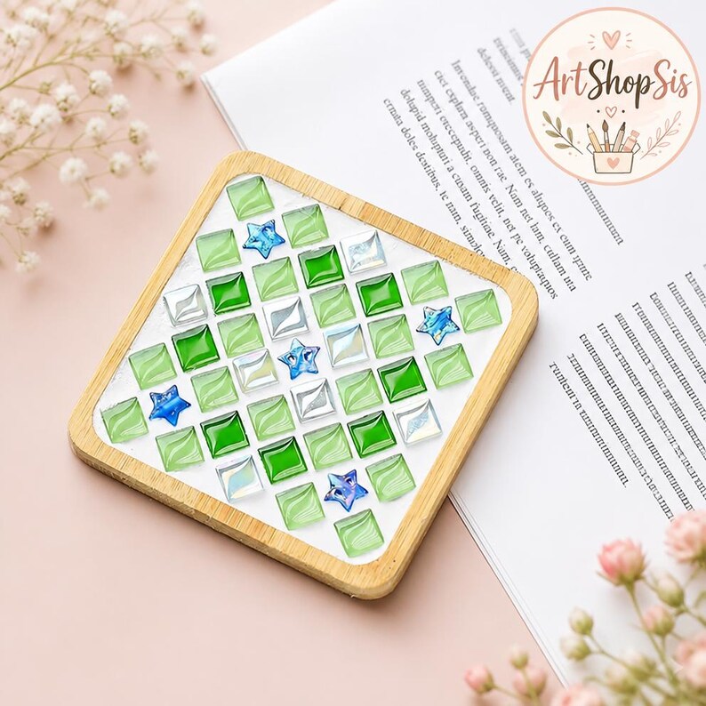 Pu&ograve; includere: Un sottobicchiere quadrato con cornice in legno chiaro caratterizzato da un motivo a mosaico di piccole tessere di vetro quadrate nei toni del verde lime, verde smeraldo e bianco iridescente, intervallate da piccole stelle di vetro blu.