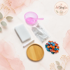 Pu&ograve; includere: Un kit per mosaico composto da una ciotola in plastica rosa con cucchiaio abbinato, una spugna rettangolare bianca, un tubetto bianco, una bustina di polvere per fughe bianca, una base rotonda in legno e tessere di vetro arancioni e blu.