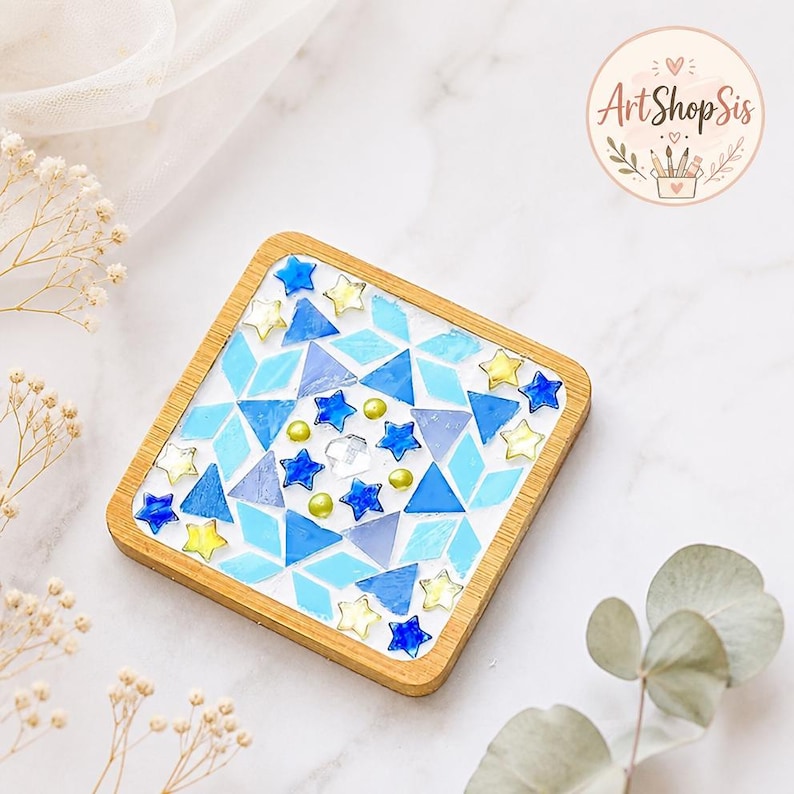 Pu&ograve; includere: Un sottobicchiere quadrato con cornice in legno caratterizzato da un design a mosaico di forme geometriche blu e azzurre, intervallate da piccoli accenti a forma di stella gialli e blu e una gemma centrale trasparente sfaccettata.