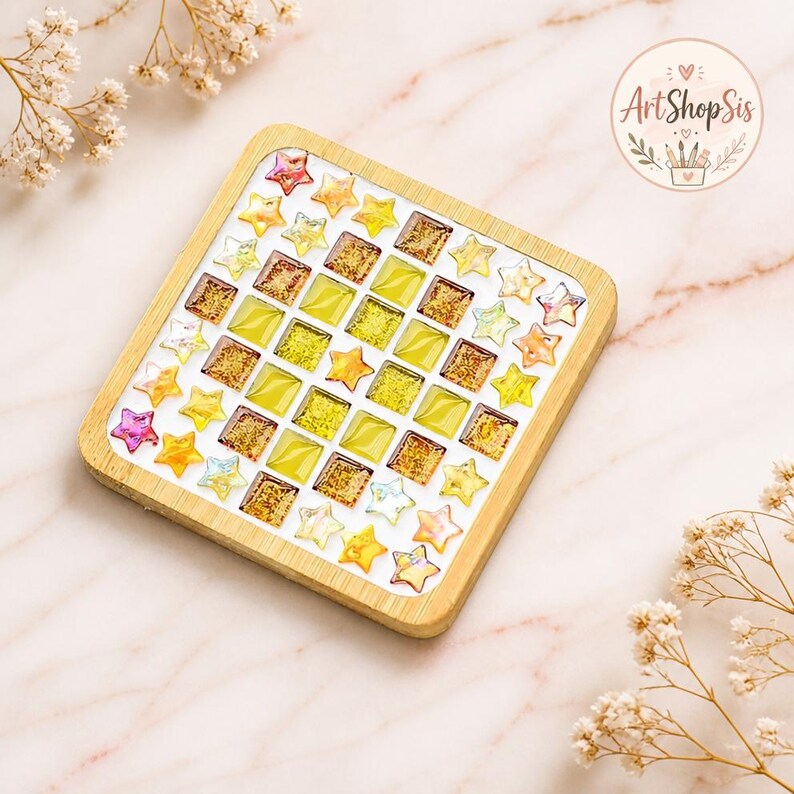 Pu&ograve; includere: Un sottobicchiere quadrato in legno con un design a mosaico di piastrelle quadrate gialle e dorate disposte a griglia, bordato da piccole tessere a forma di stella nei toni del giallo, arancione e rosa. Il logo ArtShopSis &egrave; visibile in alto a destra.