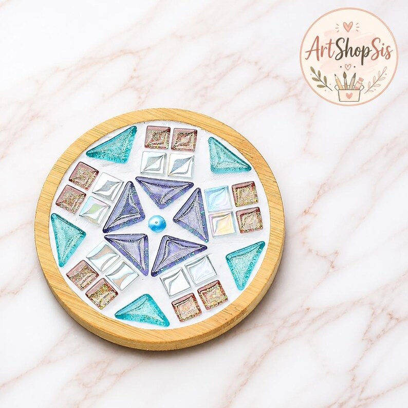 Pu&ograve; includere: Un sottobicchiere circolare in legno con un design a mosaico di tessere di vetro nelle tonalit&agrave; del viola, verde acqua e bianco iridescente. Il centro contiene una piccola perla blu circondata da pezzi di vetro geometrici a stella.