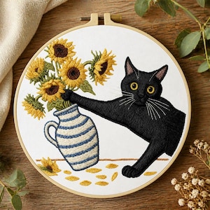Può includere: Ricamo in un cerchio di legno raffigurante un gatto nero che raggiunge un vaso di girasoli. Il vaso è a righe blu e bianche. Petali di girasole gialli sparsi. Sfondo bianco.