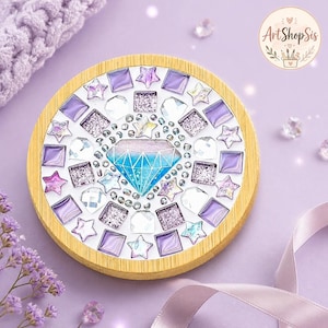 Pu&ograve; includere: Una cornice circolare in legno contenente un mosaico con un pezzo centrale a forma di diamante blu e viola, circondato da tessere quadrate e a forma di stella viola, trasparenti e glitterate, con piccole perline argentate circolari.