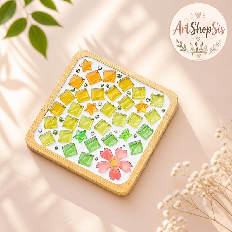 Pu&ograve; includere: Un sottobicchiere quadrato in legno con un design a mosaico composto da piccole tessere quadrate traslucide in un gradiente di giallo, lime e verde. Il motivo include diverse piccole stelle arancioni e verdi e un singolo fiore di ciliegio rosa.