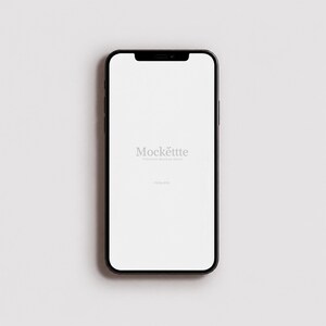 Może przedstawiać: Czarny smartfon z pustym białym ekranem z wyśrodkowanym szarym napisem Mockette Premium Mockup Store. Urządzenie posiada cienką ramkę, wcięcie na górze na aparat oraz zaokrąglone rogi, prezentowane w czystej, skierowanej do przodu orientacji.