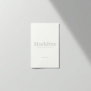 Könnte beinhalten: Eine weiße rechteckige Karte mit dem Text "Mockëttte Premium Mockup Store" in hellgrauer Schrift. Darunter steht der Text "PSD & JPEG". Die Karte befindet sich auf einem weißen Hintergrund mit Schatten.