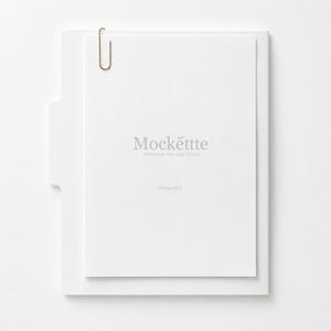 May include: A white vertical file folder containing a single sheet of white paper secured with a gold-toned metal paperclip. The paper features the centered gray text Mockette Premium Mockup Store and the smaller text PSD&JPEG below it.