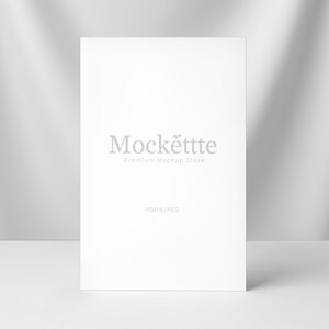 May include: A white rectangular card with the text "Mockëttte Premium Mockup Store" in gray. The words "PSD & JPEG" are printed below the text. The card is standing upright on a white surface, with shadows in the background.