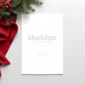 May include: A white rectangular mockup with the text "Mockëttte Premium Mockup Store" in gray. A sprig of evergreen with red berries and a red fabric are in the upper left corner. The text "PSD&JPEG" is at the bottom.