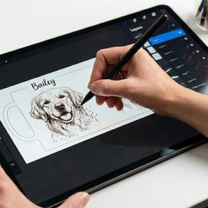 May include: A digital illustration of a Golden Retriever dog named Bailey is being drawn on a tablet with a stylus. The design is for a mug. The text "Designed by Real Artists" is in the upper left corner.