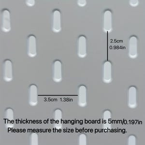 Op de afbeelding: Een wit pegboard met een herhalend patroon van verticale ovale sleuven. De verticale afstand tussen de sleuven is 2,5 cm en de horizontale afstand is 3,5 cm. De dikte van het bord is 5 mm. Tekst: The thickness of the hanging board is 5mm/0.197in. Please measure the size before purchasing.