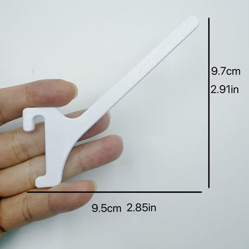 Op de afbeelding: Een witte, schuine displayhaak met een getextureerd oppervlak. Het object heeft een verticale steun met een haak aan de basis en een uitgestrekte arm. De afmetingen zijn duidelijk aangegeven als 9,7 cm in hoogte en 9,5 cm in breedte.