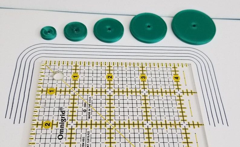 Peut inclure: Cinq cercles en plastique vert de tailles diff&eacute;rentes, avec une r&egrave;gle dans le coin inf&eacute;rieur gauche. La r&egrave;gle est gradu&eacute;e en pouces et comporte une grille.