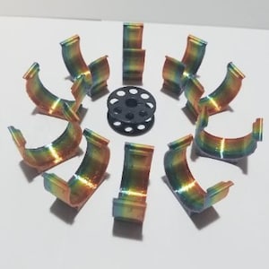 May include: Eight semi-circular clips featuring a vibrant rainbow gradient finish arranged in a circle around a single black sewing machine bobbin. Each clip has a curved profile with small protruding tabs at the top edges for secure attachment.