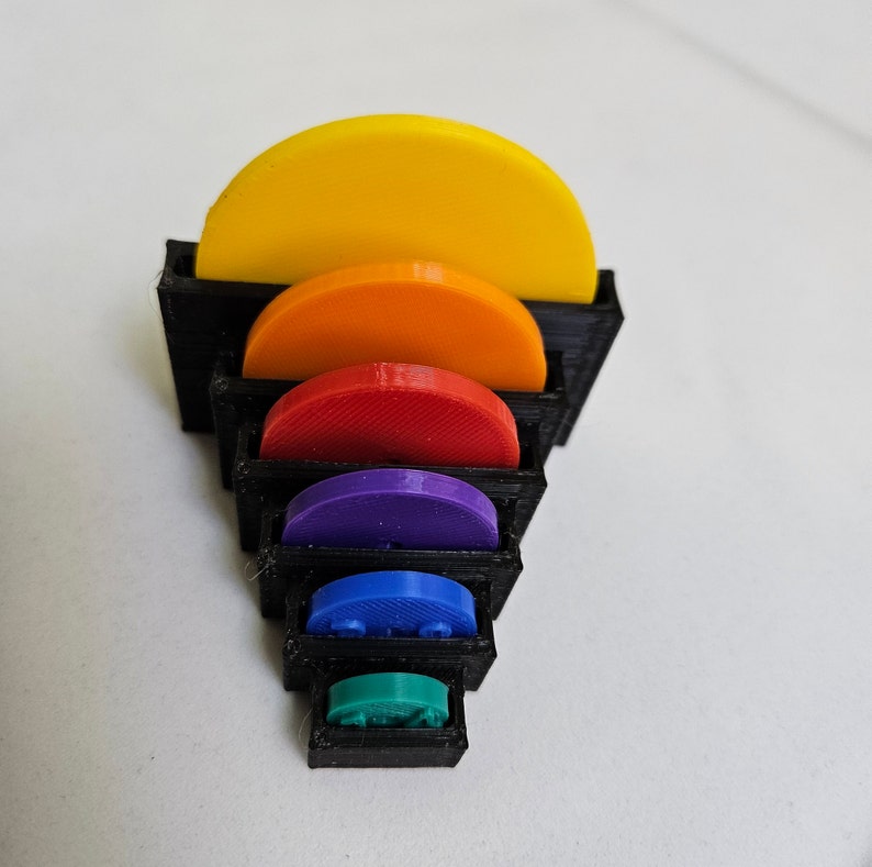 May include: A set of seven colorful, half-circle shaped pieces stacked in a black frame. The pieces are yellow, orange, red, purple, blue, green, and teal.