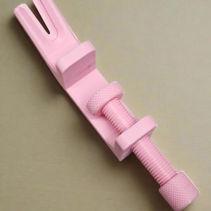 May include: A light pink C-clamp featuring a U-shaped opening at one end and a threaded screw mechanism with a textured, knurled knob for adjustment. The tool is constructed with a solid frame and a matching pink finish throughout its entire body.
