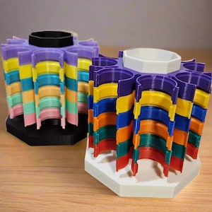 May include: Two colorful, 3D-printed organizers. One has a black base and a black center, the other has a white base and a white center. Both have a rainbow of colors, including purple, yellow, blue, orange, green, and red.