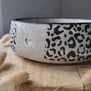 Könnte beinhalten: Eine runde Betonschale mit schwarzem Rand und herzförmigem Ausschnitt. Die Schale hat ein Leopardenmuster in Schwarz auf hellgrauem Hintergrund. Die Schale steht auf einer Holzoberfläche.