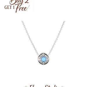 May include: A silver necklace with a circular pendant featuring a light blue center stone. The pendant is surrounded by a black and silver design. The image also includes the text "Buy 2 Get 1 Free" and the brand name "ElmareStudio".