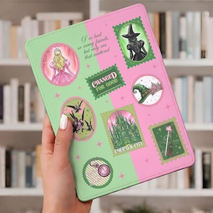 May include: A green and pink tablet case featuring illustrations and text from the Wizard of Oz. The case has a split design with stamps and quotes. The case is held in a person's hand.