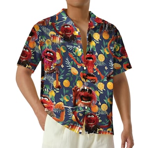 May include: Short-sleeved button-down shirt with a navy blue background featuring a repeating pattern of the Muppets' Animal character, oranges, and green leaves. The shirt has a classic collar and is unbuttoned.