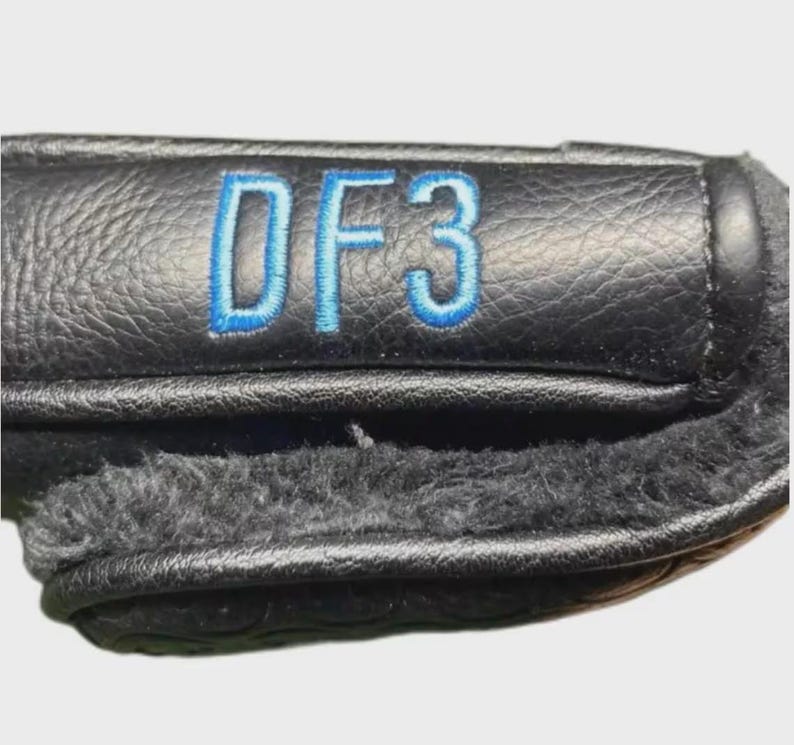 以下が含まれることがあります： 青い文字「DF3」が刺繍された黒い革製ゴルフクラブヘッドカバー。カバーの内側は柔らかくふわふわした裏地。カバーの上部は質感があります。