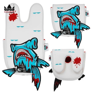 K&ouml;nnte beinhalten: Wei&szlig;e Golfschl&auml;gerhauben mit einem blauen Hammerhai-Design, roten Akzenten und einem Blutspritzer-Effekt. Die Hauben haben ein Craftsman Golf-Logo.