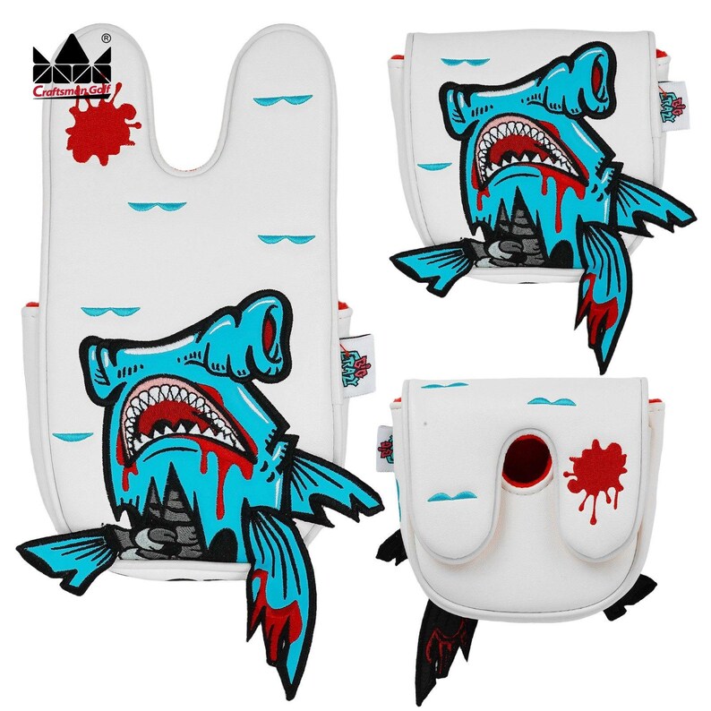 K&ouml;nnte beinhalten: Wei&szlig;e Golfschl&auml;gerhauben mit einem blauen Hammerhai-Design, roten Akzenten und einem Blutspritzer-Effekt. Die Hauben haben ein Craftsman Golf-Logo.