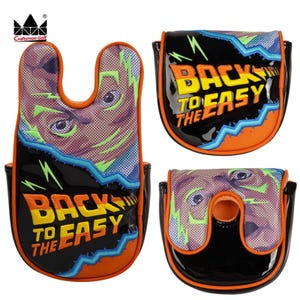 K&ouml;nnte beinhalten: Drei schwarze Golf-Putter-Schl&auml;gerhauben mit orangefarbenen und blauen Akzenten. Jede Haube zeigt den Text "BACK TO THE EASY" in Gelb und Orange sowie eine Grafik eines Gesichts. Die Hauben bestehen aus gl&auml;nzendem Material und haben ein Craftsman Golf-Logo.