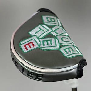 May include: A gray golf putter head cover with the word "BLUE" embroidered in white and green, with a red "E". The cover has a white and pink trim and the word "PUTTEE" is printed on the bottom.