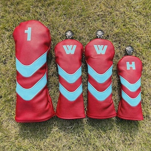 May include: Set of four golf club head covers in red with light blue chevron designs. The covers have the numbers 1, W, W, and H embroidered on them. The covers are made of a textured material and are on a green grass background.