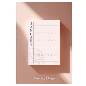 Peut inclure: Une page de calendrier rose pour janvier avec un design minimaliste. Le mot "JANUARY" est imprimé verticalement en bleu marine sur le côté gauche. La grille du calendrier est rose clair avec des lignes et des dates bleu marine. Le bas de la page porte la mention "Calender_pink type".