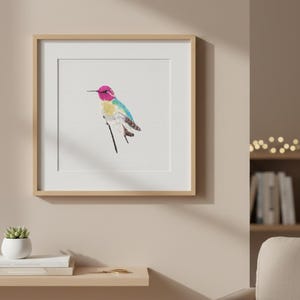 May include: A framed cross-stitch of a hummingbird. The bird has a pink head, yellow chest, and blue and green wings. The artwork is in a light wood frame and hangs on a neutral wall.