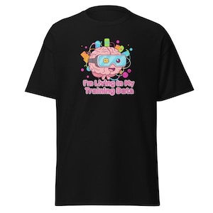 Könnte beinhalten: Schwarzes T-Shirt mit einem Cartoon-Gehirn, das eine VR-Brille trägt. Das Gehirn ist rosa mit bunten Akzenten und dem Text "I'm Living In My Training Data" in Rosa. Das Design ist mittig auf der Vorderseite des T-Shirts platziert.