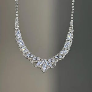 Pode incluir: Um colar prateado brilhante com cristais transparentes lapidados em marquesa. O colar apresenta uma corrente delicada e um design central de cristais maiores, criando um visual glamouroso e elegante. Perfeito para ocasiões especiais.