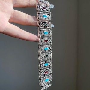 May include: Silver bracelet with rectangular links, each set with an oval gemstone in turquoise, red, green, and purple. The bracelet has an openwork design and a delicate chain fastening.