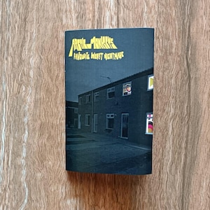 Könnte beinhalten: Dunkelblaues Albumcover mit dem Text "Arctic Monkeys" und "Favourite Worst Nightmare" in Gelb. Das Cover zeigt eine nächtliche Szene mit Häusern und beleuchteten Fenstern.