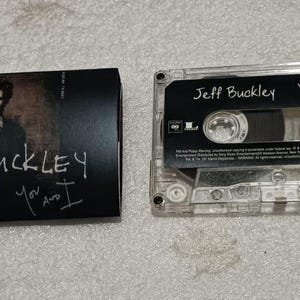 May include: A Jeff Buckley "You and I" cassette tape and its case. The case is black with a photo of Jeff Buckley and the text "Jeff Buckley You and I". The cassette is clear with black text.