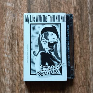 Puede incluir: Se muestra una cinta de cassette y su estuche. El estuche presenta el texto "My Life With The Thrill Kill Kult" y una imagen en blanco y negro de una mujer. La cinta de cassette es negra.