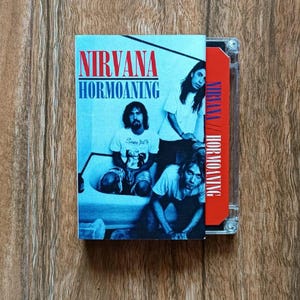 May include: A Nirvana Hormoaning cassette tape. The album cover features the band members in a bathtub. The cassette case is clear, and the tape itself is red. The album title and band name are in red and blue.