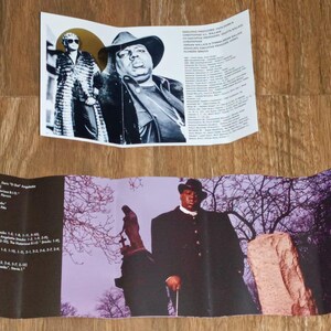 May include: A folded music album insert featuring black and white portraits of a musician in a hat and sunglasses. The insert also includes a color photo of the musician in a black coat, standing in front of a purple and gray background.