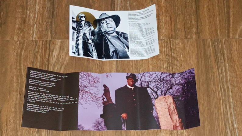 May include: A folded music album insert featuring black and white portraits of a musician in a hat and sunglasses. The insert also includes a color photo of the musician in a black coat, standing in front of a purple and gray background.