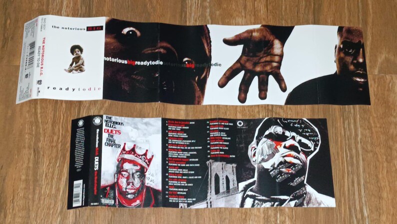 May include: Folded CD case featuring album art for "Ready to Die" and "Duets: The Final Chapter" by The Notorious B.I.G. The artwork includes portraits, a baby, and the Brooklyn Bridge. The color palette is primarily black, white, and red.