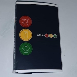 Puede incluir: Un folleto azul marino oscuro con borde blanco. La portada presenta tres iconos circulares: un avión rojo, unos pantalones amarillos y una chaqueta verde. También es visible el texto "blink-182".