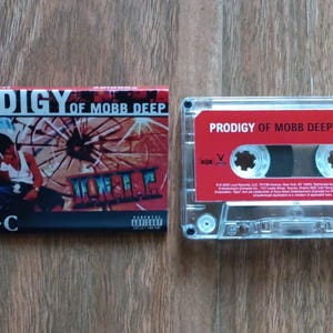 May include: A cassette tape and its case are shown. The case has the text "PRODIGY OF MOBB DEEP H-N-I-C" and an image of a person. The cassette tape is red with the same text.