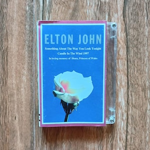 Può includere: Un'astuccio per CD con l'album di Elton John, "Something About The Way You Look Tonight." La copertina è blu con una rosa bianca e il testo "ELTON JOHN." Include anche "Candle In The Wind 1997" e una dedica alla principessa Diana.