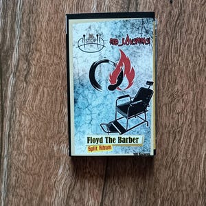 Może przedstawiać: Pudełko na płytę CD z napisem "Floyd The Barber Split Album". Okładka przedstawia fotel fryzjerski, płomień i słowa "Red Konspirasi". Tło ma wzór słojów drewna.
