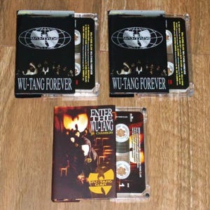 Könnte beinhalten: Drei Musikkassetten mit Albumcovern von Wu-Tang Clan. Zwei Kassetten zeigen "WU-TANG FOREVER" mit dem Wu-Tang-Logo. Die dritte Kassette zeigt "ENTER THE WU-TANG 36 CHAMBERS" mit dem Wu-Tang Clan-Logo.