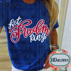 May include: A blue t-shirt with the words "Let Freedom Ring" in red and white script. The shirt has a crew neck and short sleeves. The design includes small stars.